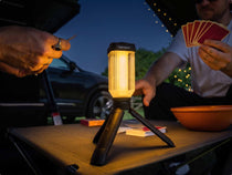 Lifestyle image showing the TentBox Tripod Light sat on a TentBox Camping Table, lighting up the area while two people play cards. 