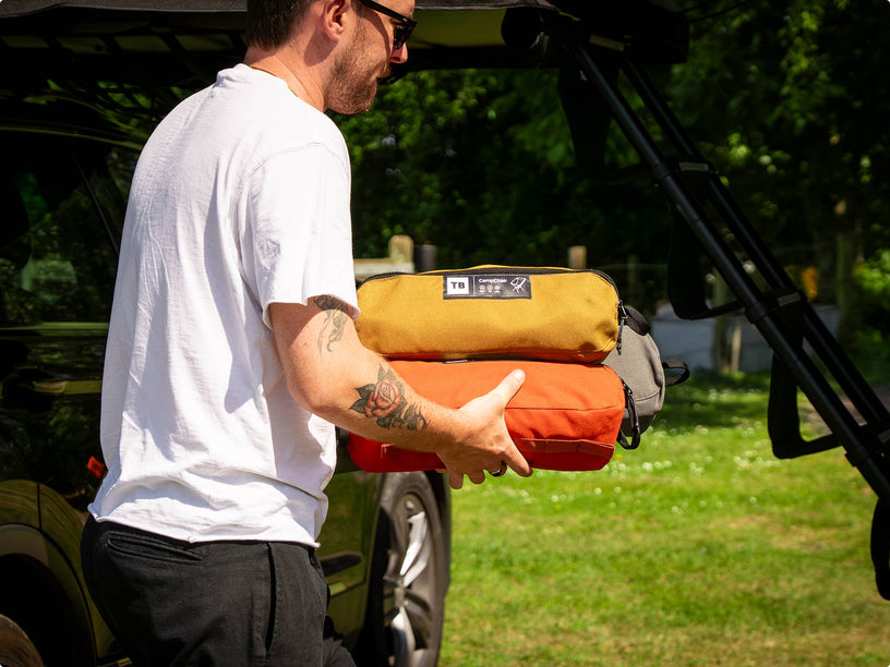 A person carrying all three colours of the TentBox Camping Chair, one of each colour, all packed into their storage bags.