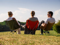 Three people sat on TentBox Camping Chairs, in red, grey and khaki
