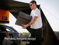 Man holding a portable, foldable TentBox solar panel near a car with a TentBox roof tent on it. 