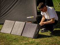 Person setting up a Tentbox solar panel on grass next to a tent