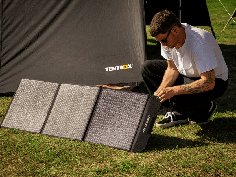 Person setting up a Tentbox solar panel on grass next to a tent