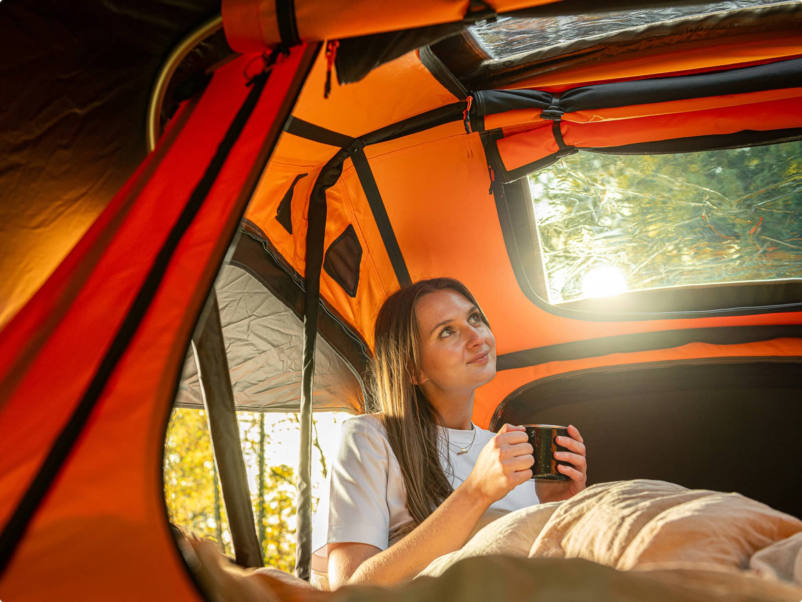 Woman inside a new Sunset TentBox Lite roof tent holding a mug, surrounded by nature.