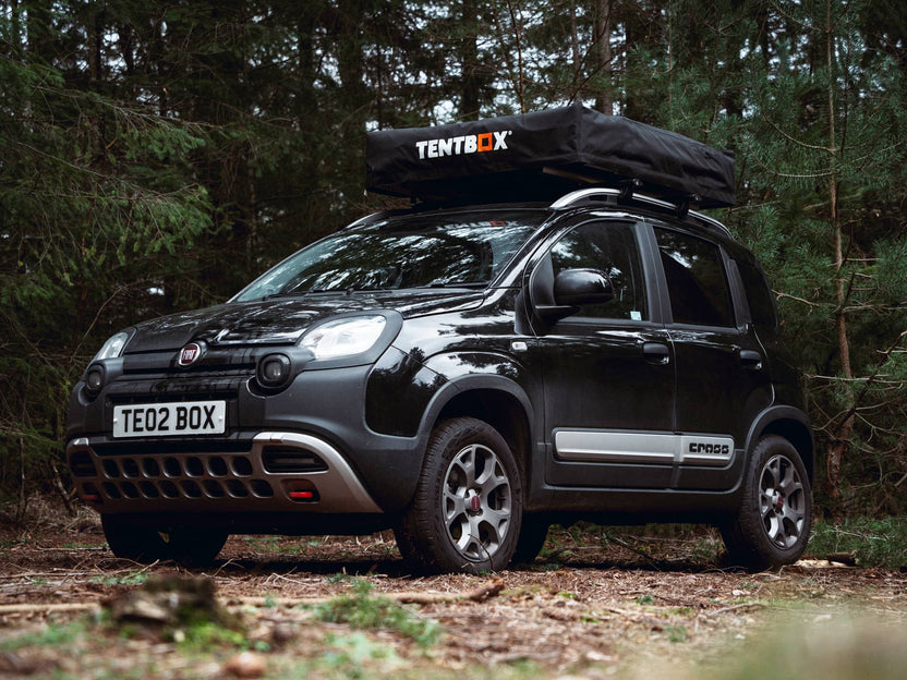 A closed TentBox Lite 2.0 roof tent installed onto a black Fiat car in the woods