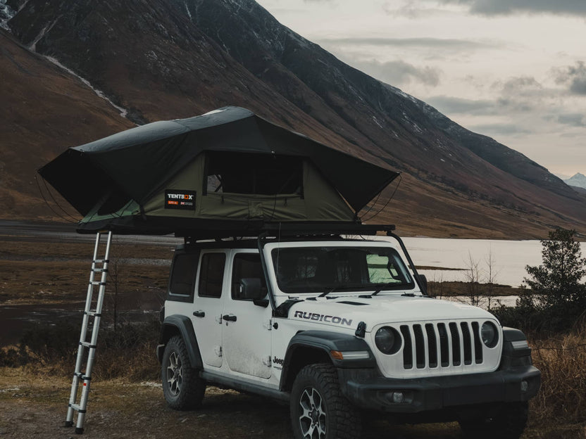TentBox Lite XL in the Forest Green colour, installed on a Jeep Wrangler that is parked in front of a Scottish mountain range.