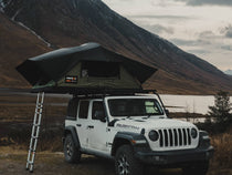 TentBox Lite XL in the Forest Green colour, installed on a Jeep Wrangler that is parked in front of a Scottish mountain range.