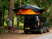 TentBox Lite XL in the Sunset Orange colour, parked by the mountain bike trails in the woods.