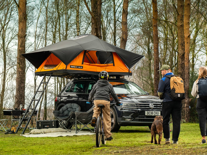The TentBox Lite XL roof tent on a car at a campsite with a family heading back to camp