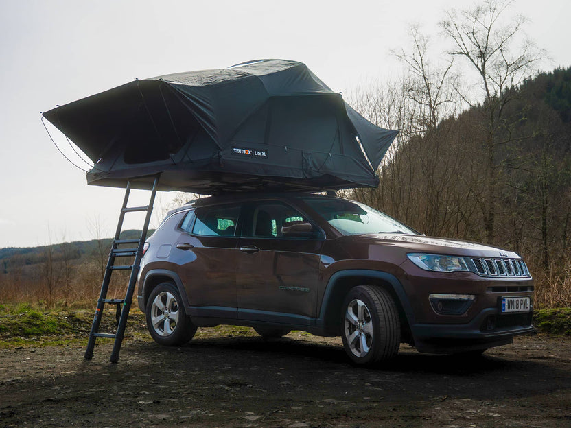The TentBox Lite XL roof tent on the roof of an SUV style vehicle in a forest setting