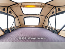 An interior view of a beige rooftop tent with a purple quilted floor mat and black support poles. The text 'Built-in storage pockets' is overlaid at the bottom.