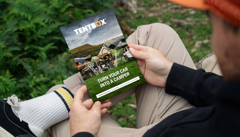Man reading TentBox roof tent brochure in camping field