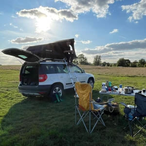 A man enjoying the views out of his TentBox GO, which is mounted on top of a white Skoda estate