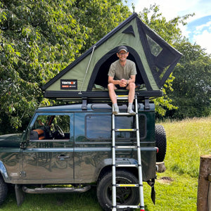 A man enjoying his camping setup with this TentBox Cargo 2.0 in Forest Green, mounted on a Land Rover Classic Defender 90