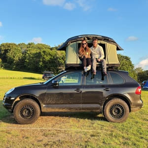 A couple enjoying the views from their TentBox Lite XL in Forest Green mounted on top of a black SUV