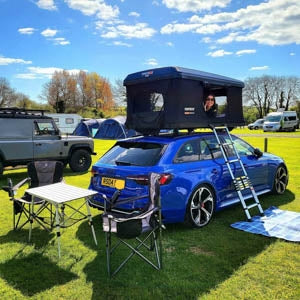 A woman looking out of her TentBox Classic 2.0 in Midnight Grey at the campsite