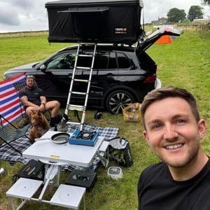 A man taking a selfie in front of his camp with a TentBox Classic 2.0 in Midnight Grey in the background